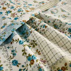 Extreme close-up of the cotton fabric, showing the intricate detail of the blue floral and plaid patchwork pattern.