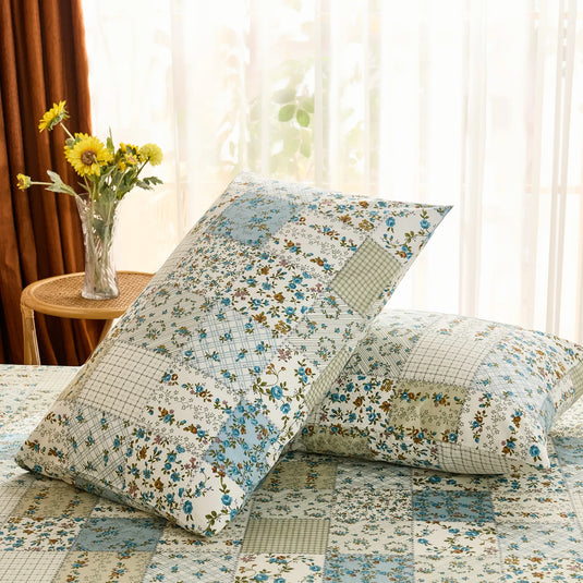Two cotton pillowcases in a cottage-style patchwork print, brightly lit by natural light near a window.