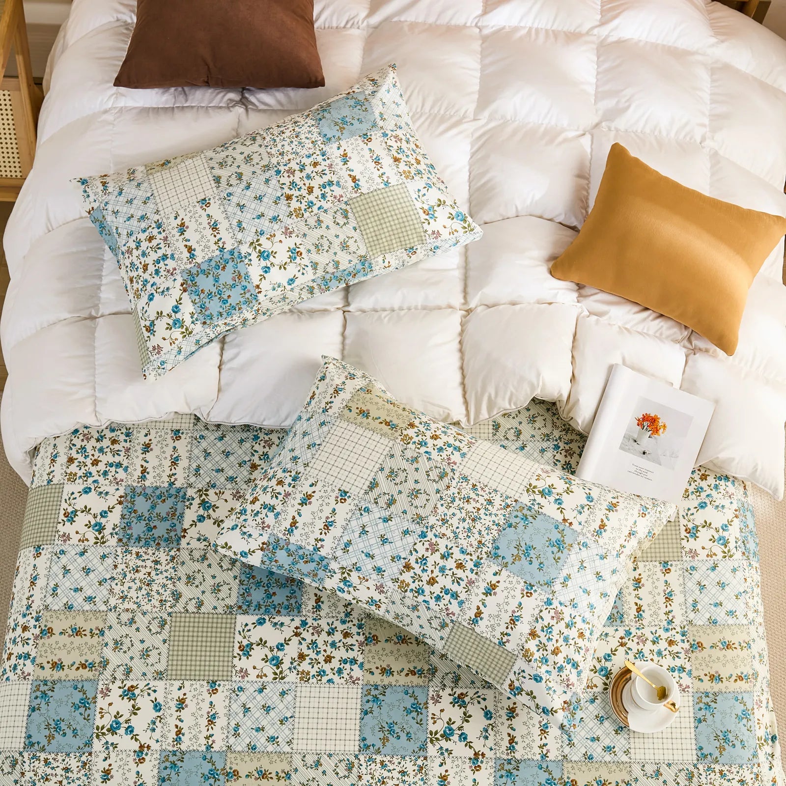 Overhead shot of two cotton patchwork pillowcases and a matching sheet set on a white quilted duvet.
