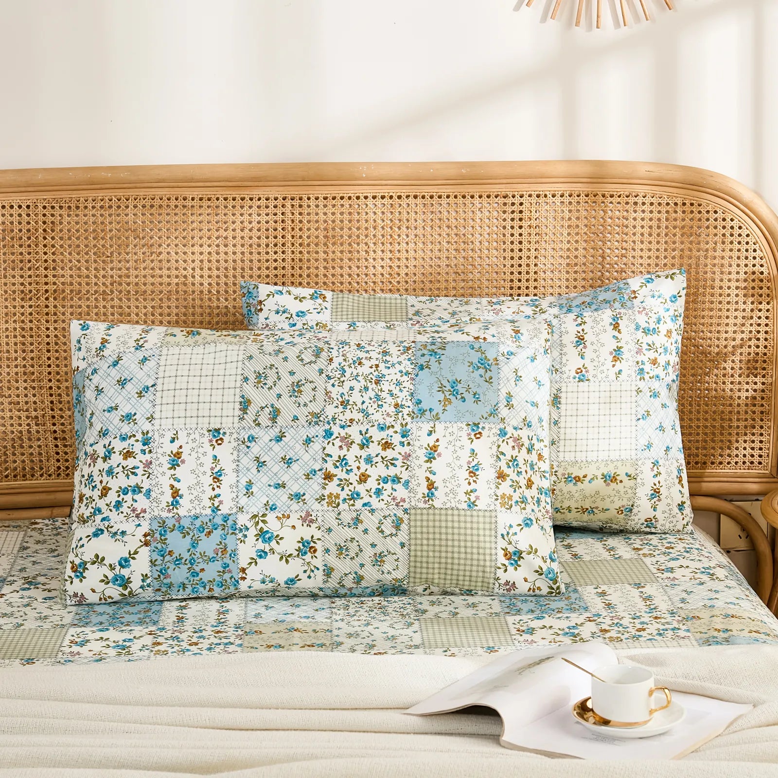 Two cotton pillowcases with a blue floral and white plaid patchwork design displayed on a bed with a rattan headboard.