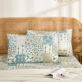 Two cotton pillowcases with a blue floral and white plaid patchwork design displayed on a bed with a rattan headboard.