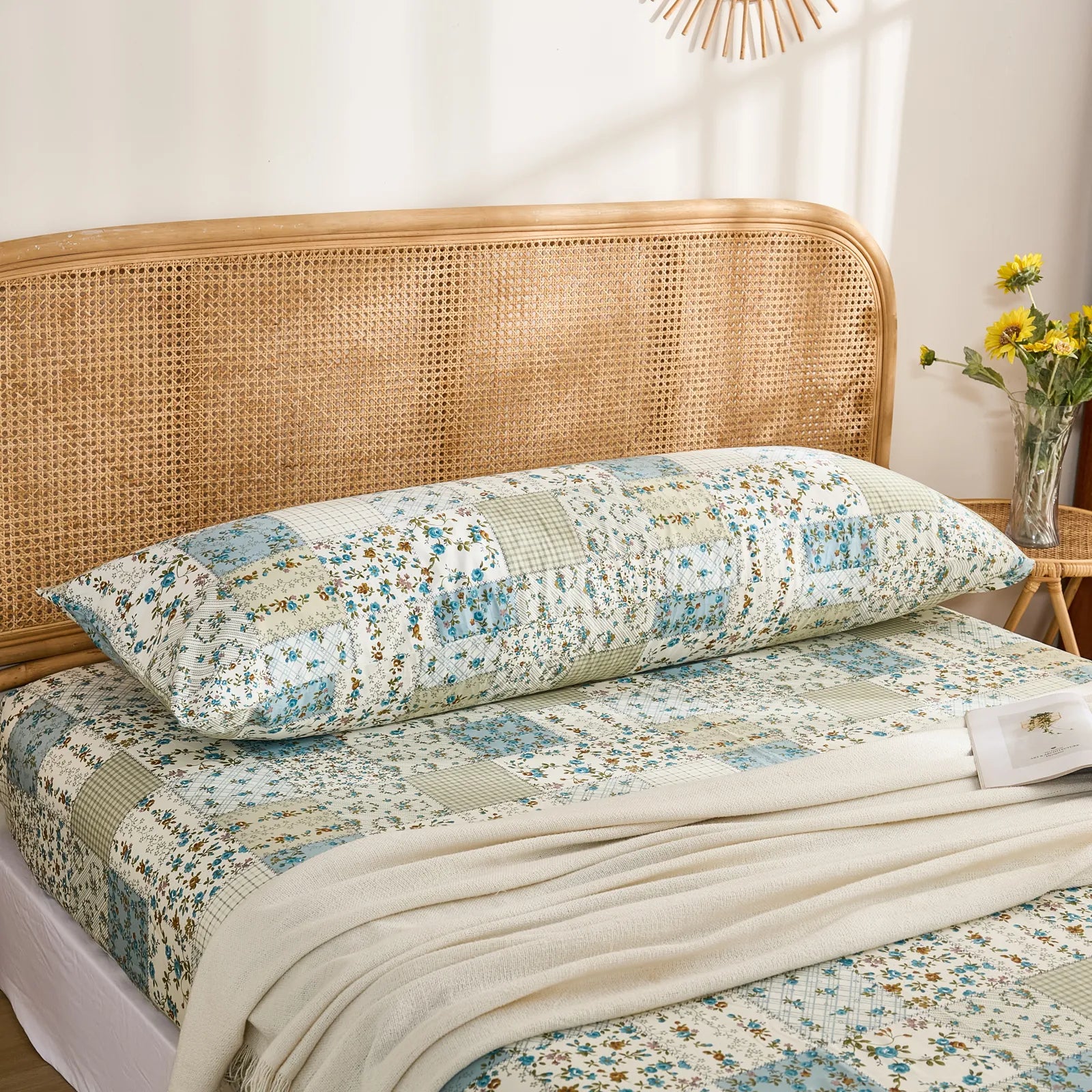 The cotton body pillowcase with a blue floral patchwork print styled on a bed with a rattan headboard.