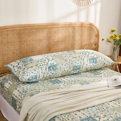 The cotton body pillowcase with a blue floral patchwork print styled on a bed with a rattan headboard.