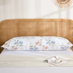 The cotton blue floral body pillowcase placed horizontally against a rattan headboard, perfect for a modern cottage look.