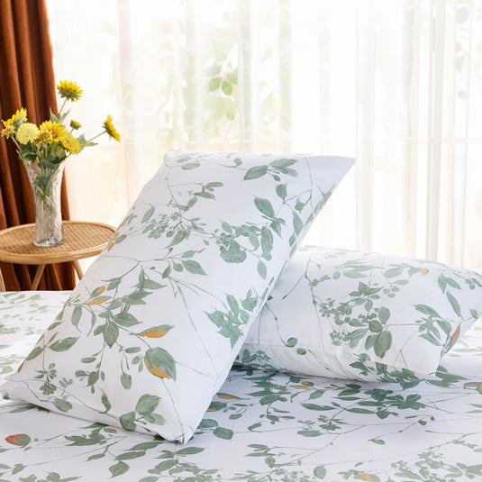 Two cotton pillowcases with a watercolor-style green leaf print, shown in bright natural light by a window.