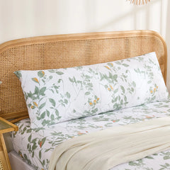 Full front view of a long cotton body pillowcase with a watercolor-style green leaf print, resting against a rattan headboard.