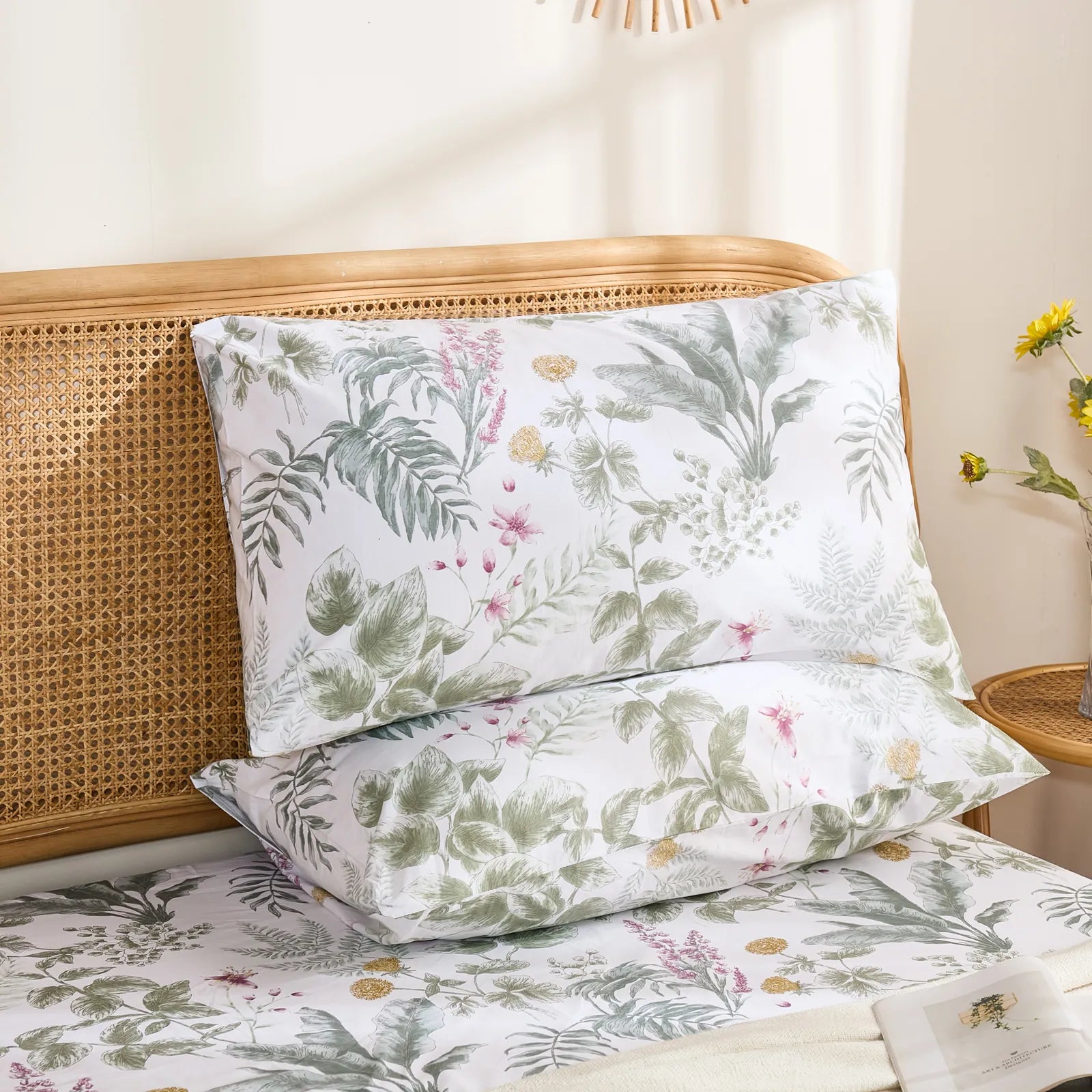 Two cotton pillowcases featuring a detailed tropical leaf and flower pattern, stacked on a bed in a bright setting.