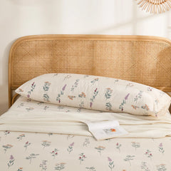 The long cotton body pillowcase resting against a rattan headboard, showing the full botanical print.