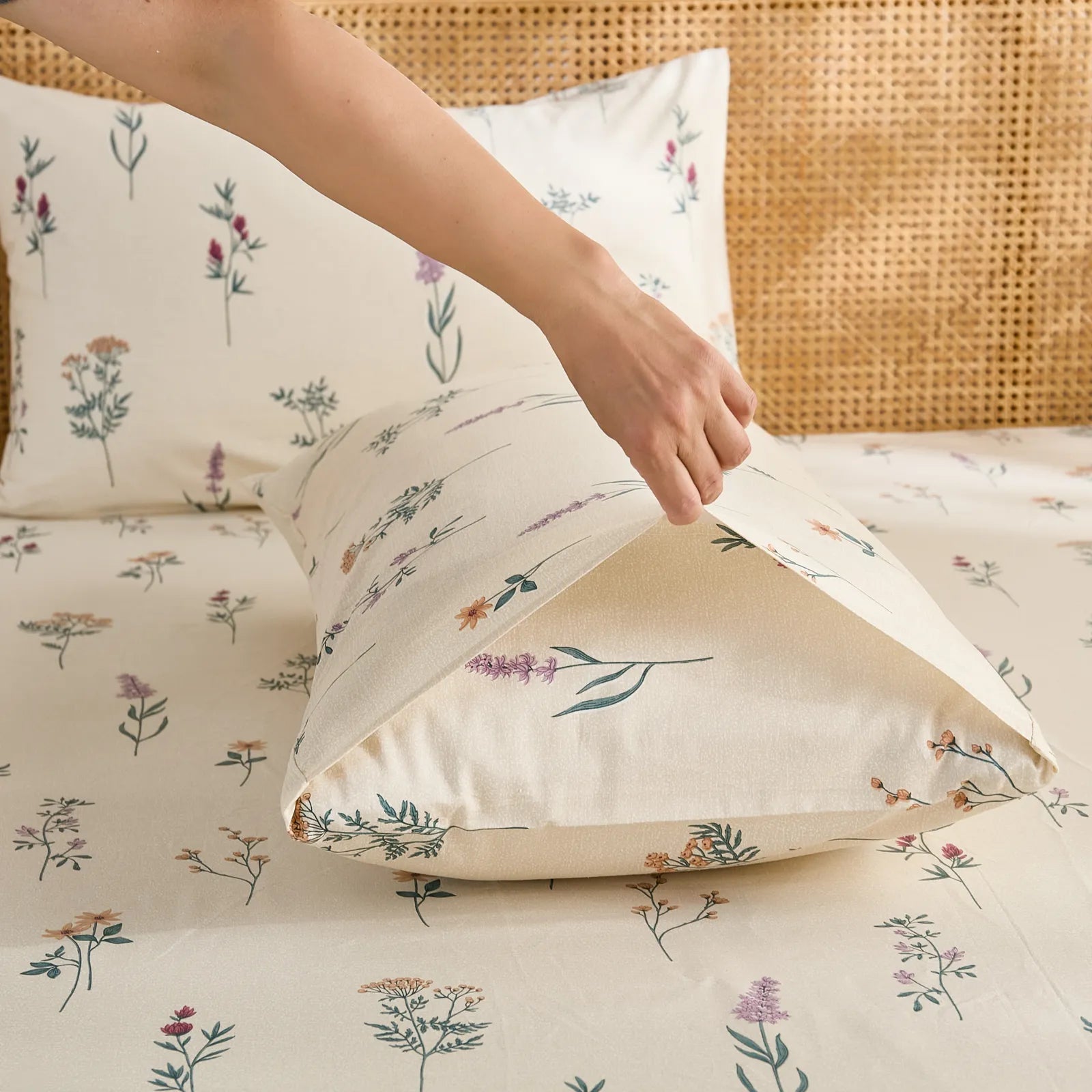 A hand tucking in a pillow into the cotton pillowcase, showing the envelope closure detail and wildflower print.