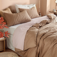 Headboard view of beige camel duvet cover with subtle pink trim, wicker table and red leaves.