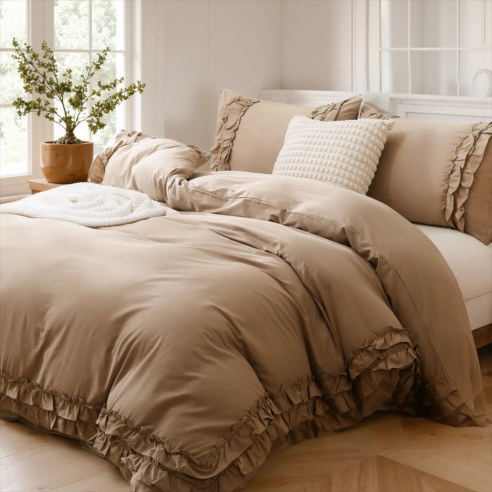 Beige cotton double ruffle duvet cover set with a grid-pattern pillow and a plant in a terracotta pot.
