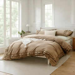 Beige cotton ruffle duvet cover and pillows on a bed with a draped throw blanket, near a large sunny window.