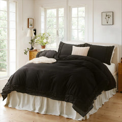 Black cotton double ruffle bedding set on a bed between nightstands with a fruit bowl and wall art.