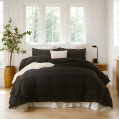 Black cotton double ruffle duvet cover with pillows, a wood planter, and a black lamp on a nightstand.