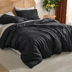 Corner perspective of black duvet with single pillow arrangement, woven basket and plants on light wood floor.