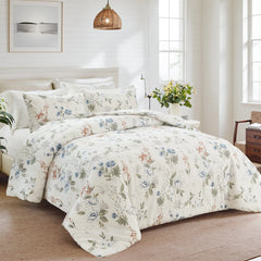 Bed with white floral comforter set in a bright bedroom with a woven light fixture and large windows.