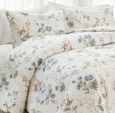 Close-up, corner view of a bed with a white comforter and pillows featuring a blue and orange floral pattern.