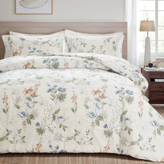 Full shot of a bed with a white floral comforter set, wood headboard, and a lamp on the nightstand.
