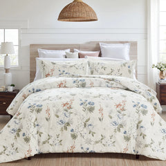 Bed with white floral comforter and pillows in a rustic bedroom with wood headboard and nightstand.