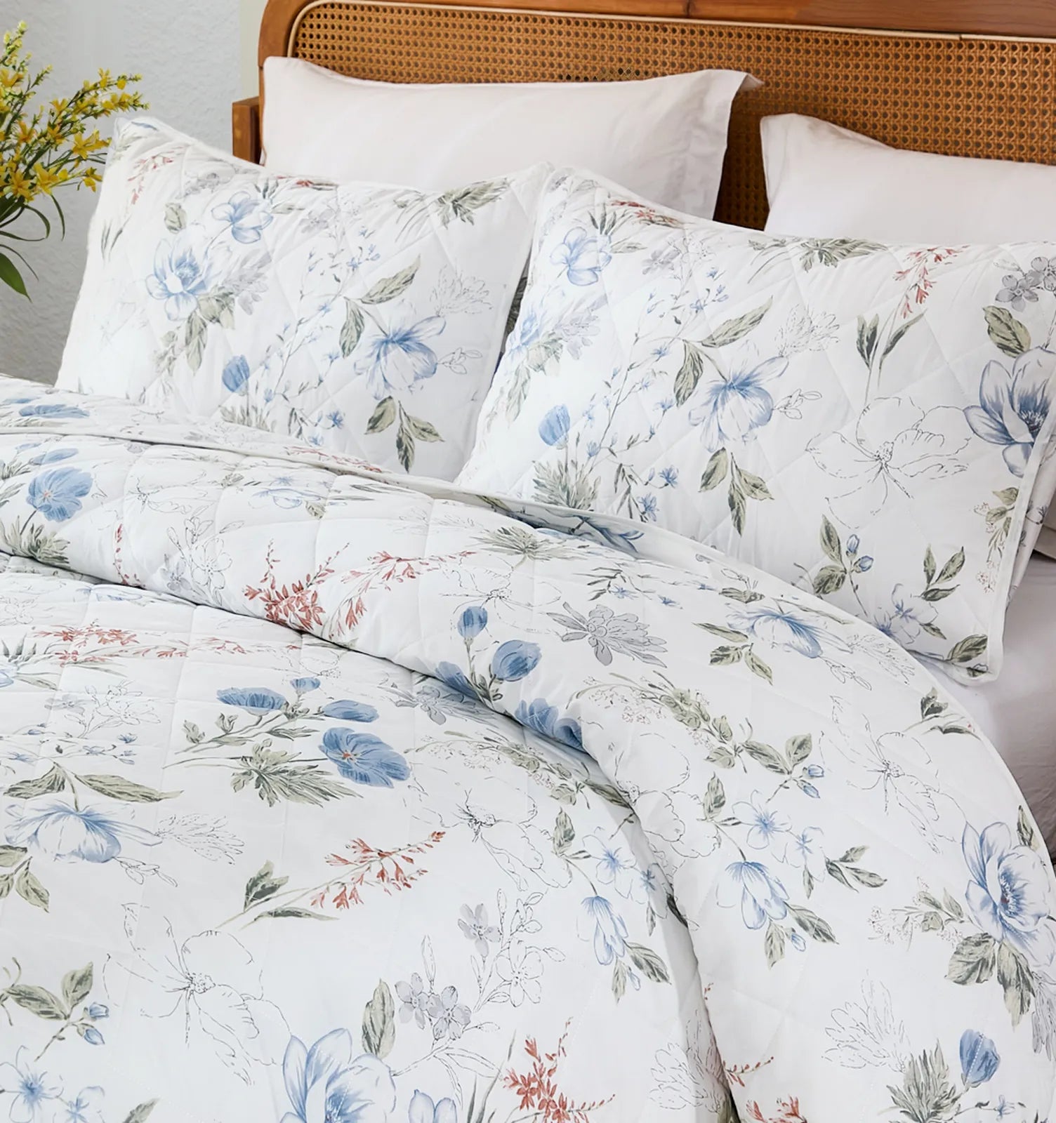 Close-up of the bed, showing the white quilt and pillows with a delicate blue floral pattern.