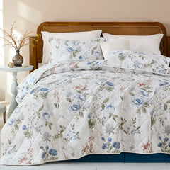 Bed with white and blue floral quilt set in a bright bedroom with a rattan headboard and blue-toned rug.