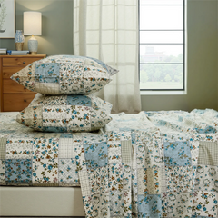 Stacked blue and green floral patchwork cotton pillows on the fitted sheet set close up