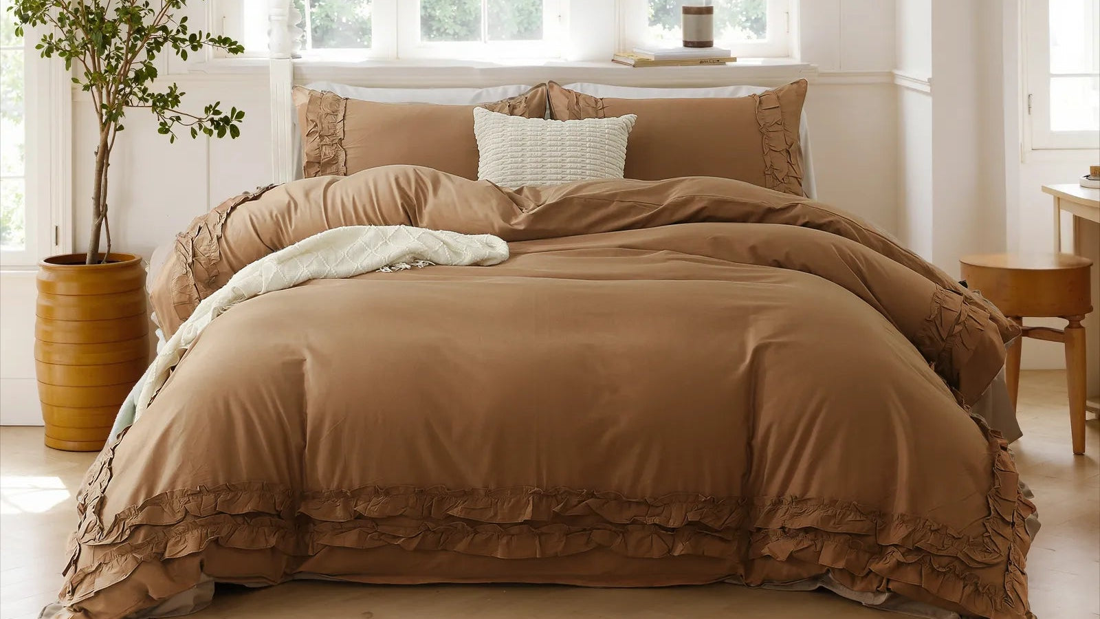Brown cotton double ruffle duvet cover set with a white pillow, beside a cylindrical planter and a white lamp on a wooden stool.