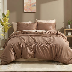 Front view of brown cotton duvet with brown and pink pillows against abstract wall art with green plants on both sides.