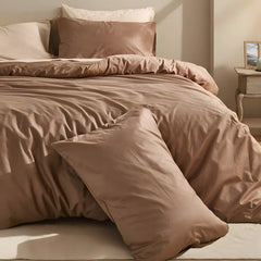Brown duvet with white and brown pillows in slanting sunlight with simple nightstand arrangement.