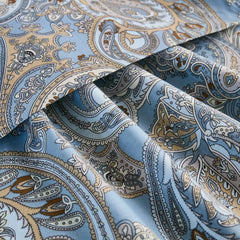 A close-up of the folded light blue cotton fabric, showcasing the detailed and intricate paisley pattern with brown and white accents.