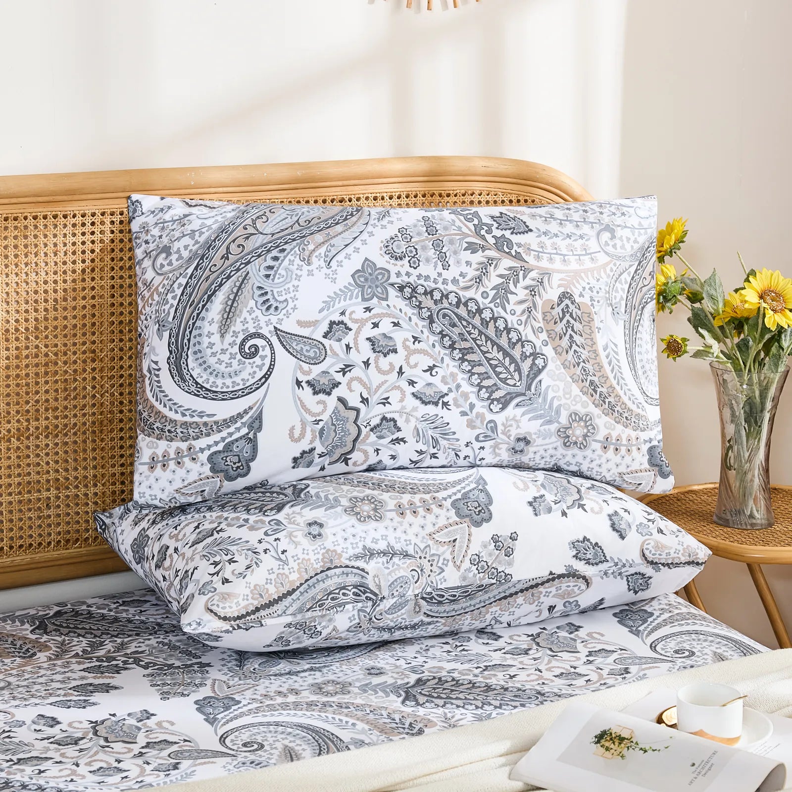 A flat-lay photo of two cotton grey paisley pillow shams and a matching sheet, shown on a white quilted duvet with small accent pillows.