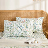 Two cotton meadow flower pillowcases are neatly arranged on a bed with a rattan headboard, styled with a book and a teacup.