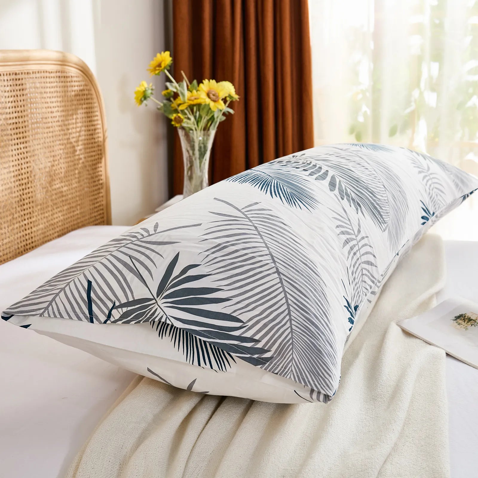 A side-angled view of a tropical palm leaf cotton body pillowcase on a bed, showing the end of the pillowcase and the woven rattan headboard.