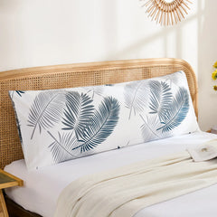 A cotton body pillowcase featuring a tropical palm leaf print, styled horizontally on a bed with a rattan headboard and a decorative vase.