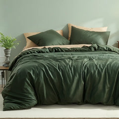 Overhead view of dark green cotton duvet with light beige pillow contrast, beside wooden table with plant.