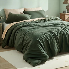 Side angle view of dark green duvet with layered pillows between symmetrical nightstands with decor.