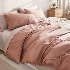 Angled overhead view of a dusty pink cotton duvet set with white sheets, beside a nightstand with books and metal decor.
