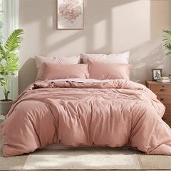 Front view of a dusty pink cotton duvet with layered pillows, under a pink floral art piece on a light wall.