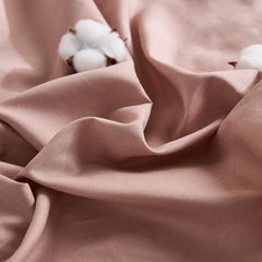 Close-up of dusty pink solid duvet fabric with two cotton blooms on wrinkled surface