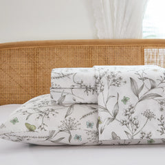 Close up stack of folded cotton botanical fitted sheet and pillowcases with window light