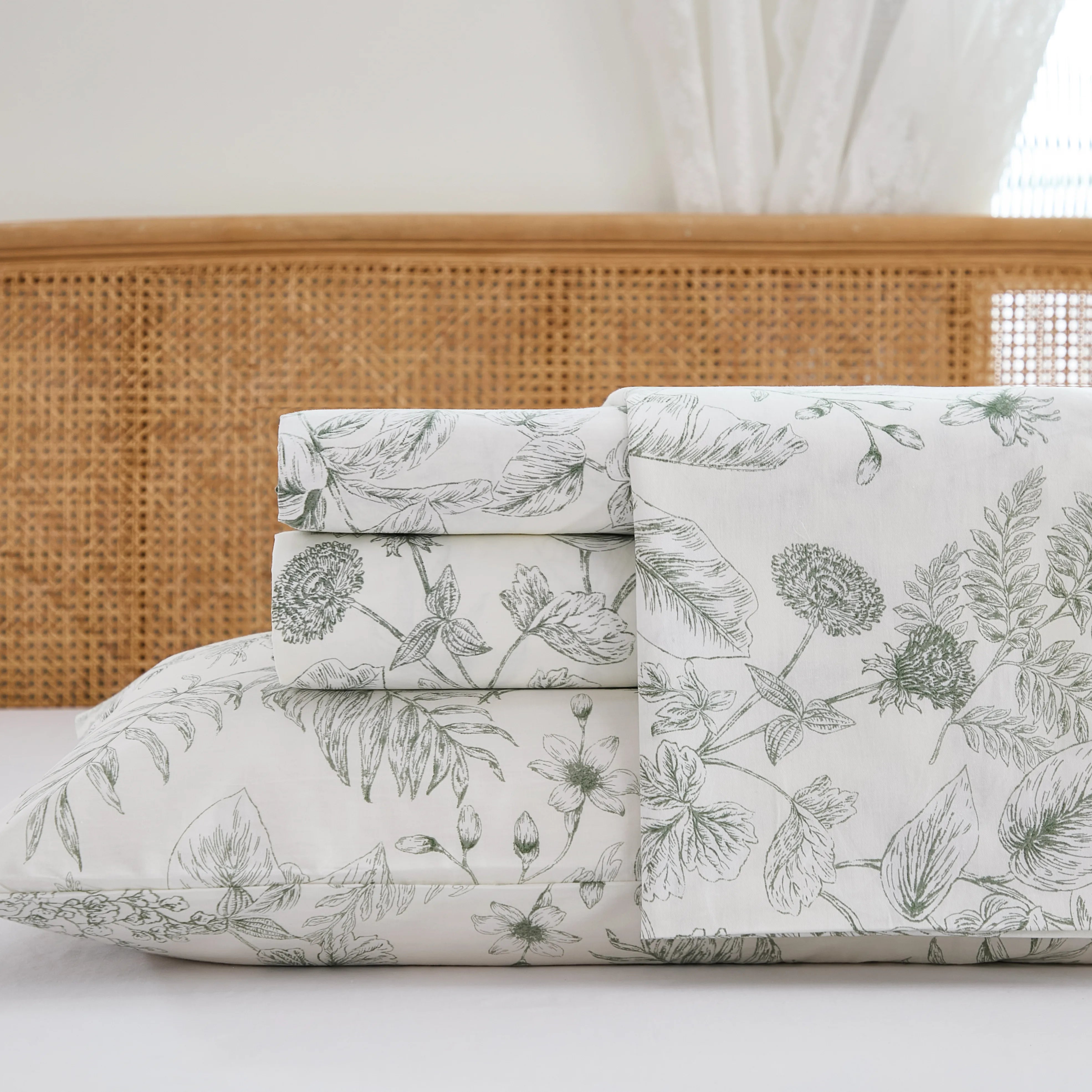 Close up stack of folded cotton greenery fitted sheet and pillowcases on white background