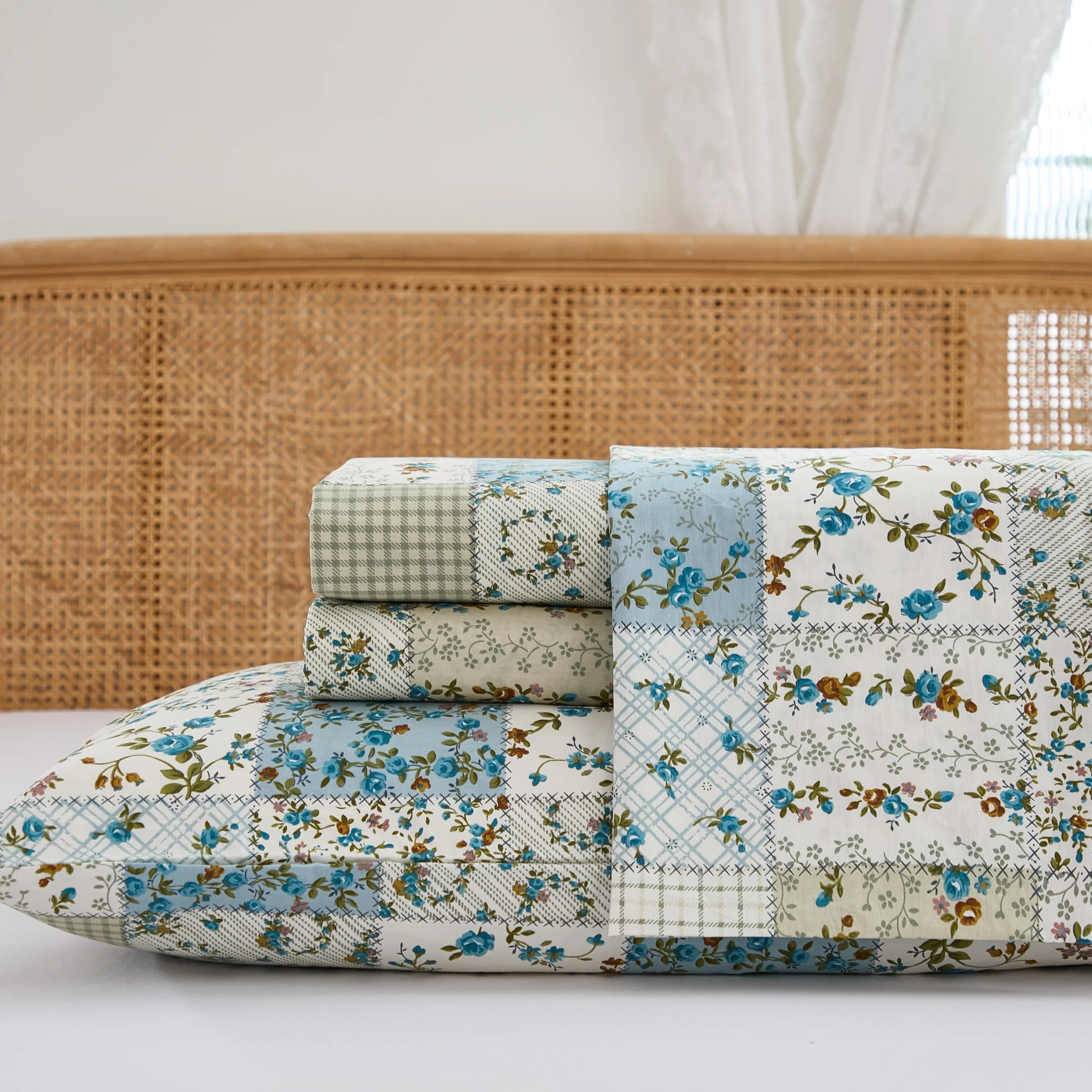 Close up stack of folded cotton patchwork fitted sheet and pillowcases with rattan headboard