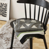 A neatly folded geometric throw blanket with green and black borders sits on a modern black chair.