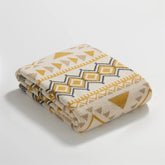 Neatly folded mustard yellow cream and gray boho geometric knit blanket studio shot