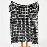 A person holding up the full-sized artistic black and white wool blanket to display the complete, abstract grid pattern.