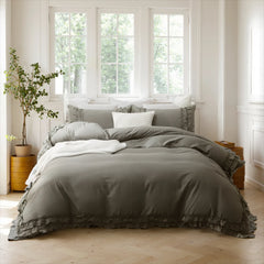 Gray cotton double ruffle duvet cover on a bed with pillows, beside a yellow planter and three large sunny windows.