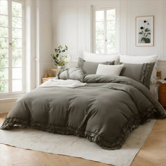 A bed with a gray cotton duvet cover and pillows, flanked by two nightstands with plants, under a botanical print.