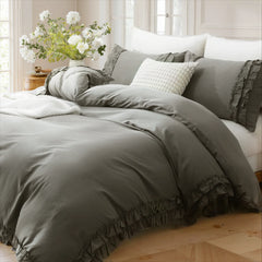 Gray cotton ruffle bedding on a bed with a wooden side table holding a vase of fresh white flowers.