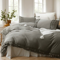 Angled view of a gray cotton ruffle duvet cover set with a white knit blanket and a view of trees.