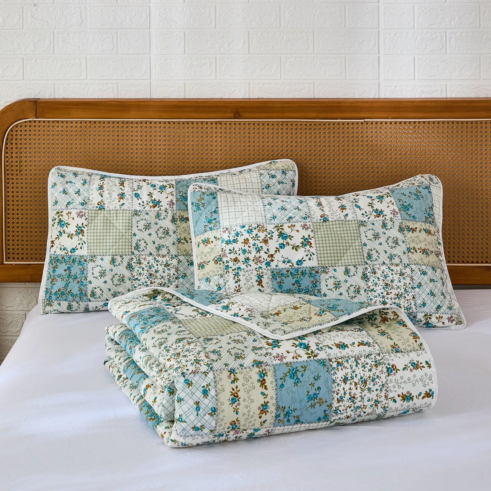 Two pillows and a folded quilt from the green and blue patchwork set on a white bed.